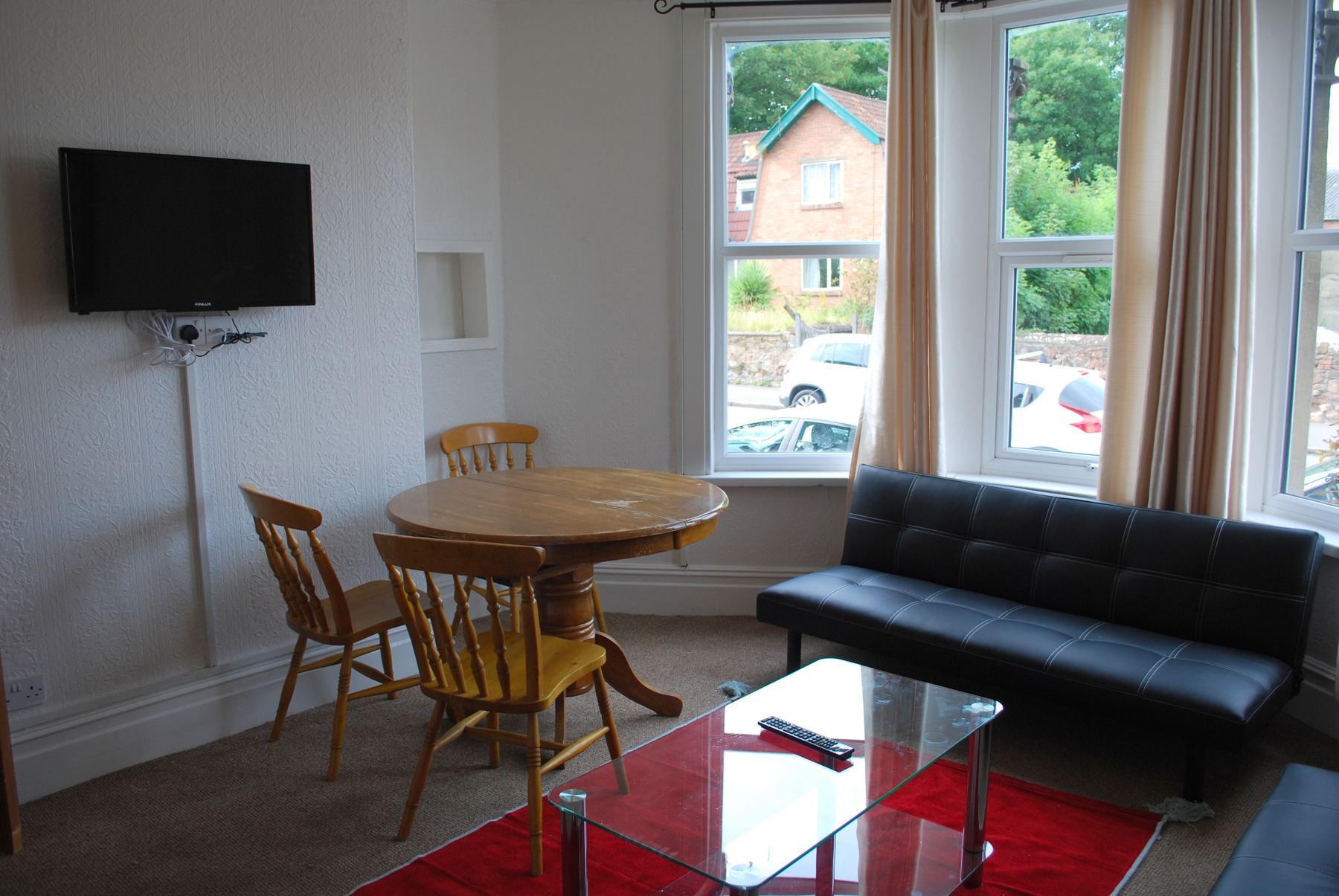The guest lounge with a round dining table, leather sofa, red rug and big bay window